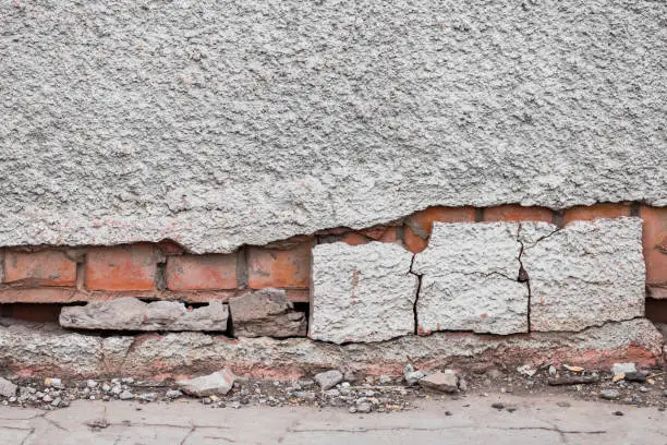 The foundation of a residential building is gradually collapsing. Cracks in the foundation. Plaster falling off of a brick wall due to the impact of weather factors.
