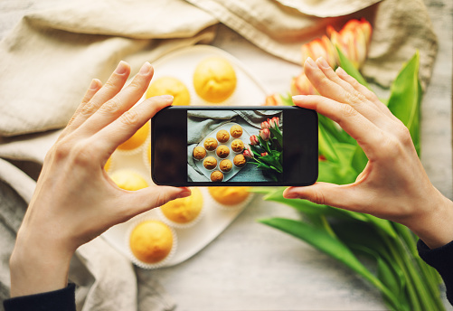 Woman taking photo of cupcakes with smartphone