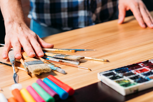 Artist tools. Paints paintbrushes markers arrangement. Man at workplace. Art studio. Creative process occupation lifestyle.