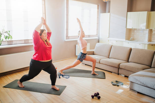 istock Youbng plus size model and well-built woman doing exercise together. Stretching up and standing in yoga pose. Asana meditation. Workout for two in living room. 1148839885