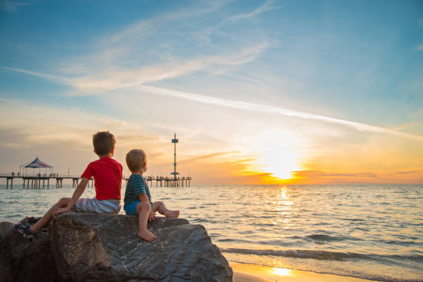 istock Two boys sitting on the rock at the beach at sunset 1148840788