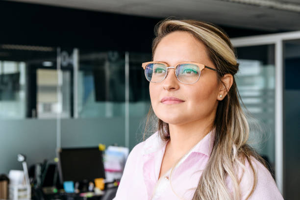 Mid adult businesswoman wearing glasses Portrait of woman in her 30s in modern office, looking away, contented expression, contemplation looking away stock pictures, royalty-free photos & images