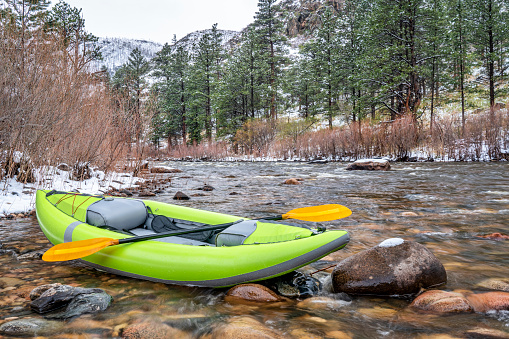 inflatable whitewater kayak with a paddle on shore of mountain river after springtime snowstorm - Poudre River in northern Colorado