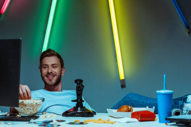 istock handsome and smiling man looking at computer monitor and eating popcorn 1148844192