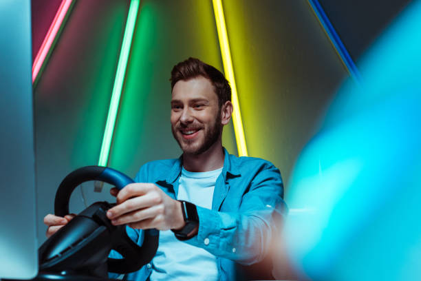 istock selective focus of handsome and smiling man playing video game with steering wheel 1148844225