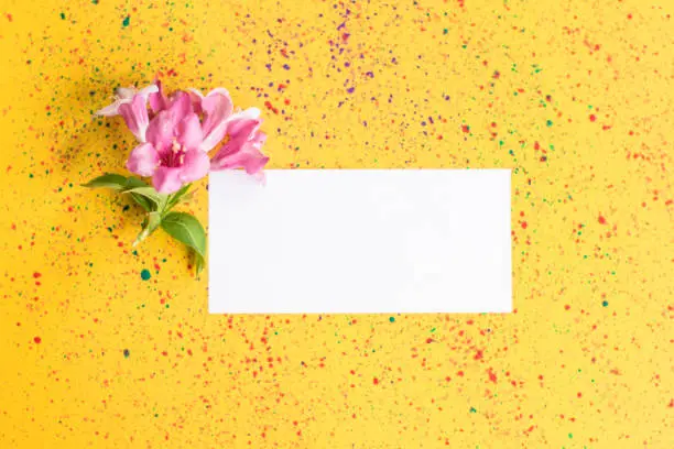 Photo of Feminine wedding desktop mock-up with blank paper card and spring pink flowers on yellow colorful shabby table background. Empty space. Styled stock photo, web banner. Flat lay, top view