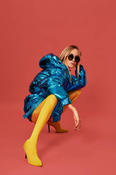 istock Young confident blonde girl in blue jacket squats in studio before camera, red background 1148853620