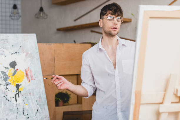 istock selective focus of handsome artist with paintbrush looking at canvas 1148855933