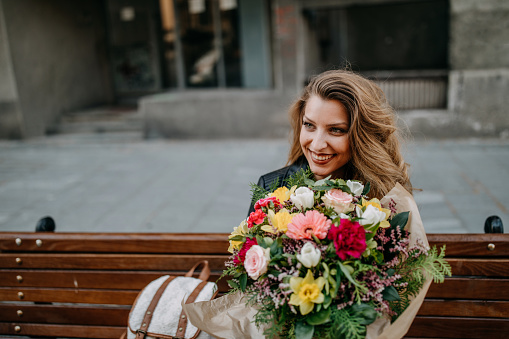 Young woman sitting on the bench with flower bouquet