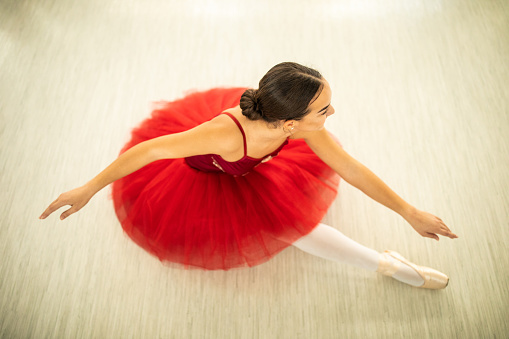 Cheerful teenage ballet dancer sitting on floor , wearing red elegant dress,, directly above