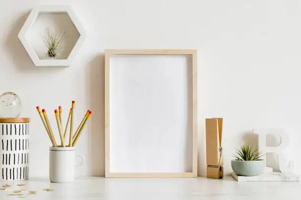 Photo of Modern and stylish home interior with wooden mock up poster frame, design office accessories, tapes, supplies, notes, memo sticks, air plants. Scandinavian home decor. Minimalistic concept. Template.