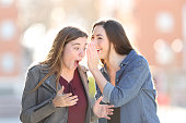 Gossip woman telling secret to her surprised friend