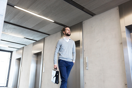 Confident businessman with briefcase walking in lobby at office