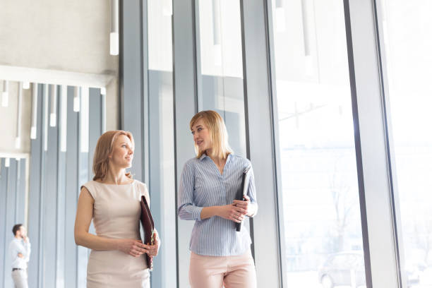 istock Businesswomen with files talking while walking in corridor by office 1148873928
