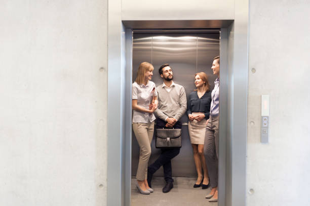 collègues parlant tout en restant dans l’ascenseur au bureau - elevator photos et images de collection