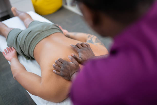 istock Dark-skinned therapist massaging back for man in shorts 1148876651