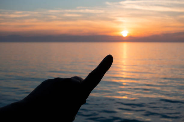 istock Silhouetted hand pointing up towards a sunset over the horizon at sea 1148880109