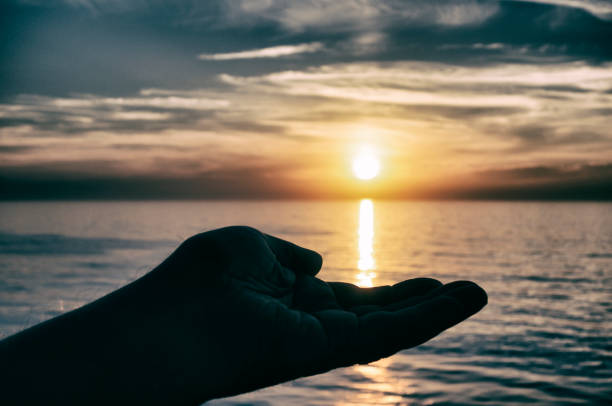 istock Mysterious man's silhouetted hand cupping a sunset at sea 1148880283