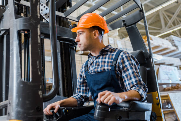 istock warehouse worker in uniform and helmet operating forklift machine 1148880371