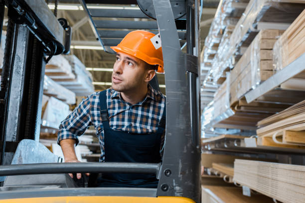 istock attentive warehouse worker in uniform and helmet operating forklift machine 1148880374