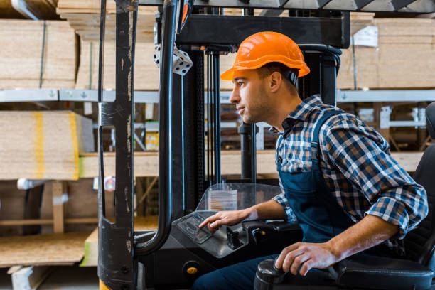 istock concentrated handsome worker in uniform and helmet operating forklift machine 1148880375