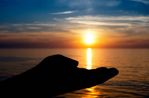 istock Man's silhouetted hand cupping a sunset at sea 1148880643