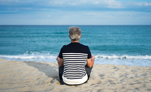 Senior man meditating on the beach, summer vacation workout