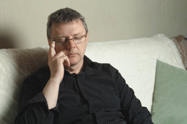 A tired man with glasses is sitting on the sofa.