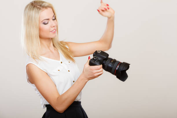 Photographer girl shooting images. Attractive blonde woman taking photos with camera, on gray background