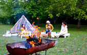 Fire flame in barbecue grill close up and family people background in green nature