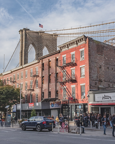 New York City, USA - Oct. 19, 2018: people walking past shops in streets of Brookly, with Brooklyn Bridge in background