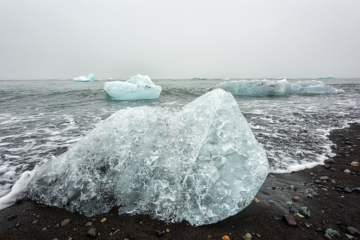 Ice crystal on the famous black sand beach and ocean waves, a part of icebergs from Jokulsarlon glacier lagoon, Diamond beach on the south coast of Iceland