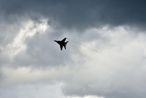 Black silhouette of a fighter plane against the sky with clouds