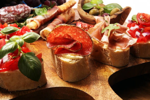 istock Traditional italian antipasto bruschetta appetizer with cherry tomatoes, cream cheese, basil leaves and balsamic vinegar on cutting board with prosciutto, salami, cheese 1148897909