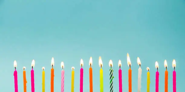 Photo of Set of many different color shape and pattern birthday candles burning isolated on blue. Happy Birthday card design concept.  Bottom lower border edge a lot of copy space.