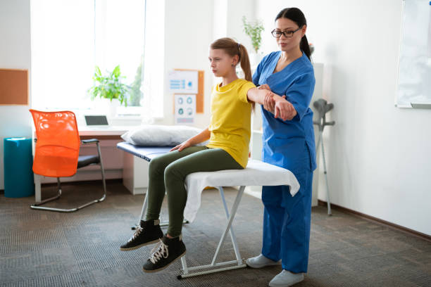 Focused dark-haired professional nurse stretching hand of her patient Uncomfortable young girl. Focused dark-haired professional nurse stretching hand of her patient while she sitting on covered daybed sports physical stock pictures, royalty-free photos & images