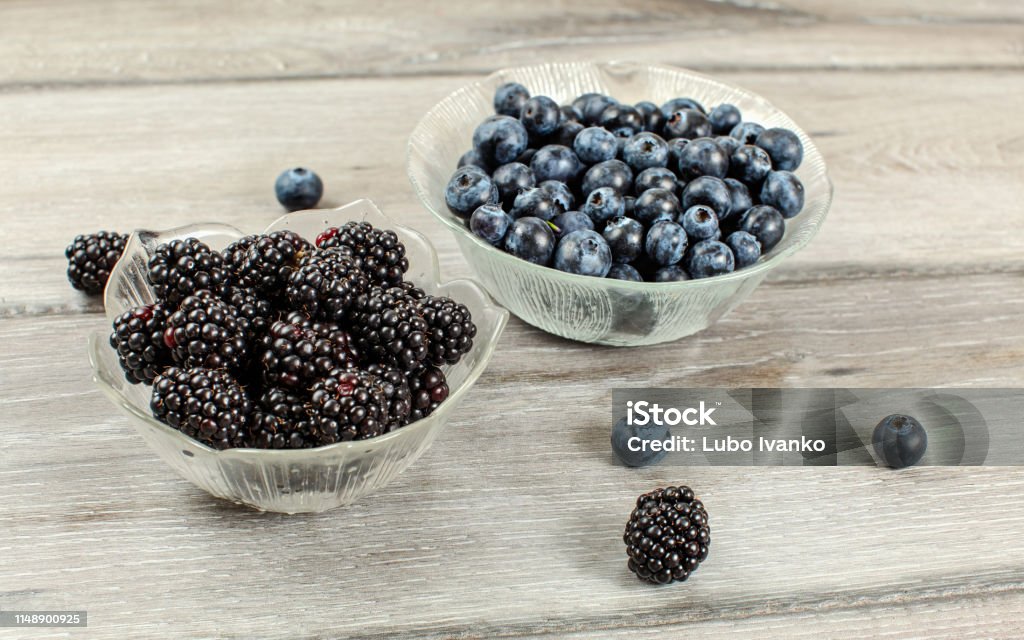 Small glass bowl of blueberries and blackberries on gray wood desk Backgrounds Stock Photo