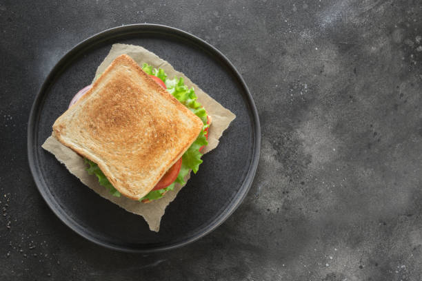 istock Sandwich with bacon, tomato, onion, salad on black background. Isolated. View from above. 1148902588