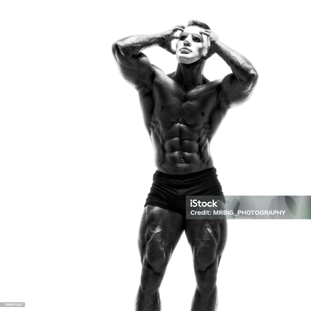 Mysterious Muscular man hiding behind white mask. Bodybuilder with white mask on his face. Studio shot on white background Actor Stock Photo