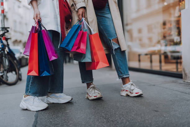 Young women with shopping bags standing on the street Look what we bought. Close up of two girl in jeans and sneakers holding colorful shopping bags merchandise stock pictures, royalty-free photos & images