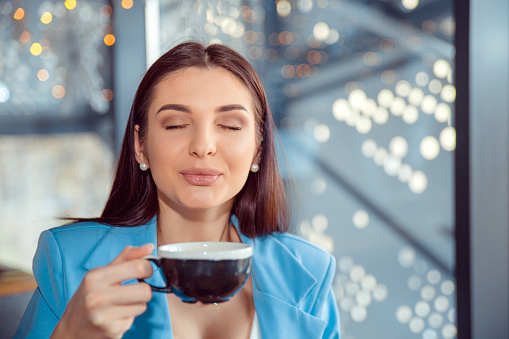 Love for coffee. Portrait of cute girl drinking enjoying her tea in the living room in manhattam apartment home or a fancy cafe, wearing blue suit, white shirt, having breakfast with pleasure relaxing