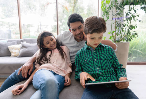 istock Dad, daughter and son relaxing on couch while looking at a video on tablet all smiling 1148934426