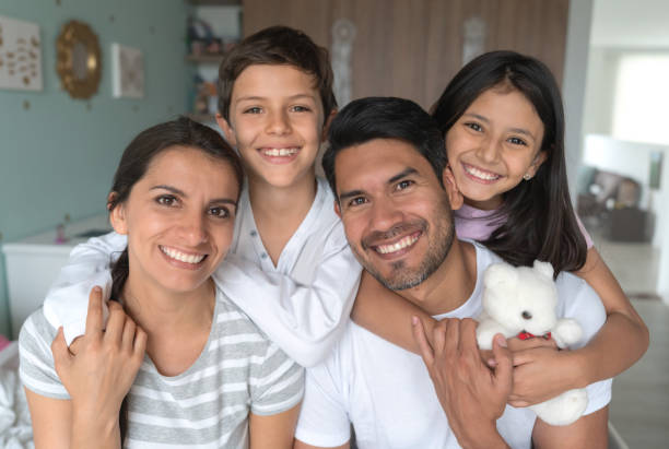 istock Beautiful couple with their two kids ebracing each other while facing camera smiling at home 1148934434
