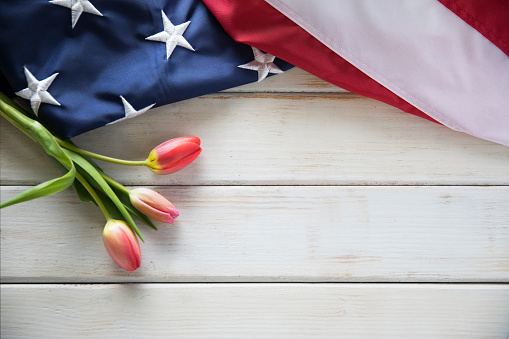 This is a close up photo of an American flag on and old retro white wooden table with red tulips. This is a great image for memorial day, veterans Day, etc.