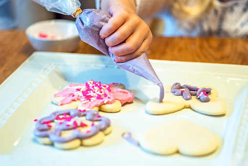 Closeup of child decorating sugar cookies with piping bag filled with purple frosting