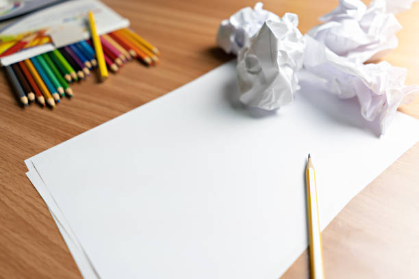 Colored and crumbled papers on a table, there are a pencil, eraser and a sharpener