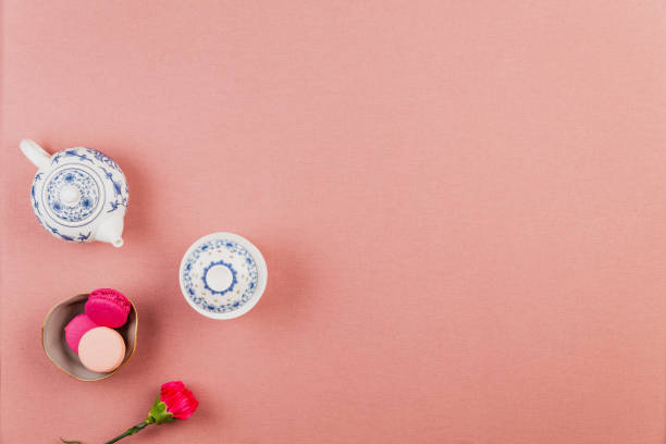 Pink and fuchsia french macarons or macaroons, in a bowl with fuchsia incarnation flower and chinaware teapot and bowl over a pink tablecloth background with copyspace. stock photo