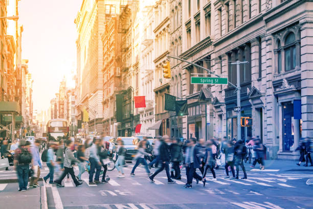 People walk across the crowded intersection of Broadway and Spring Street in New York City Diverse groups of people walk across the crowded intersection of Broadway and Spring Street in the SoHo neighborhood of Manhattan in New York City with bright sunlight background soho new york stock pictures, royalty-free photos & images