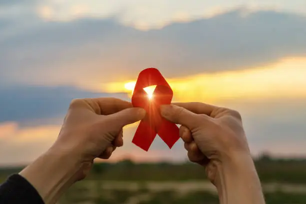 Photo of Aids red ribbon in hands .