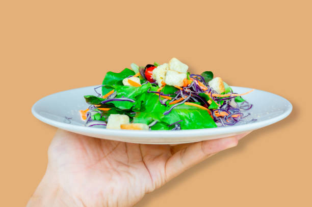 istock Hands holding a white dish with fresh salad, with a brown backdrop 1148972829